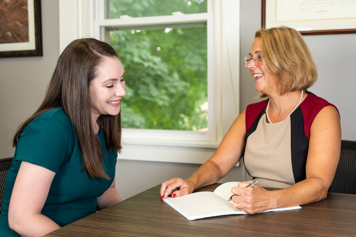 Two women sitting at a desk as one writes in a notebook